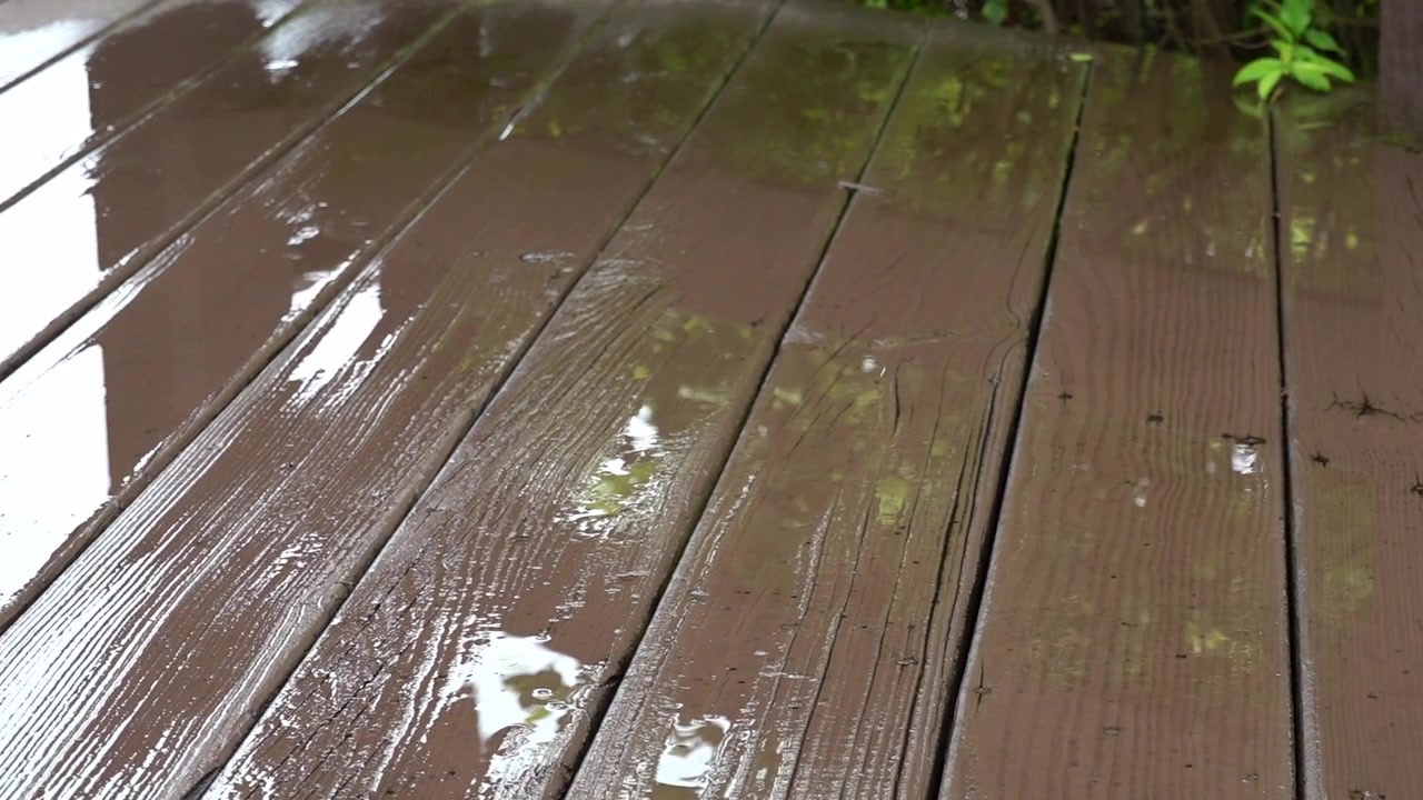 Primo piano di gocce di pioggia che cadono su una superficie di legno bagnata durante una forte pioggia.