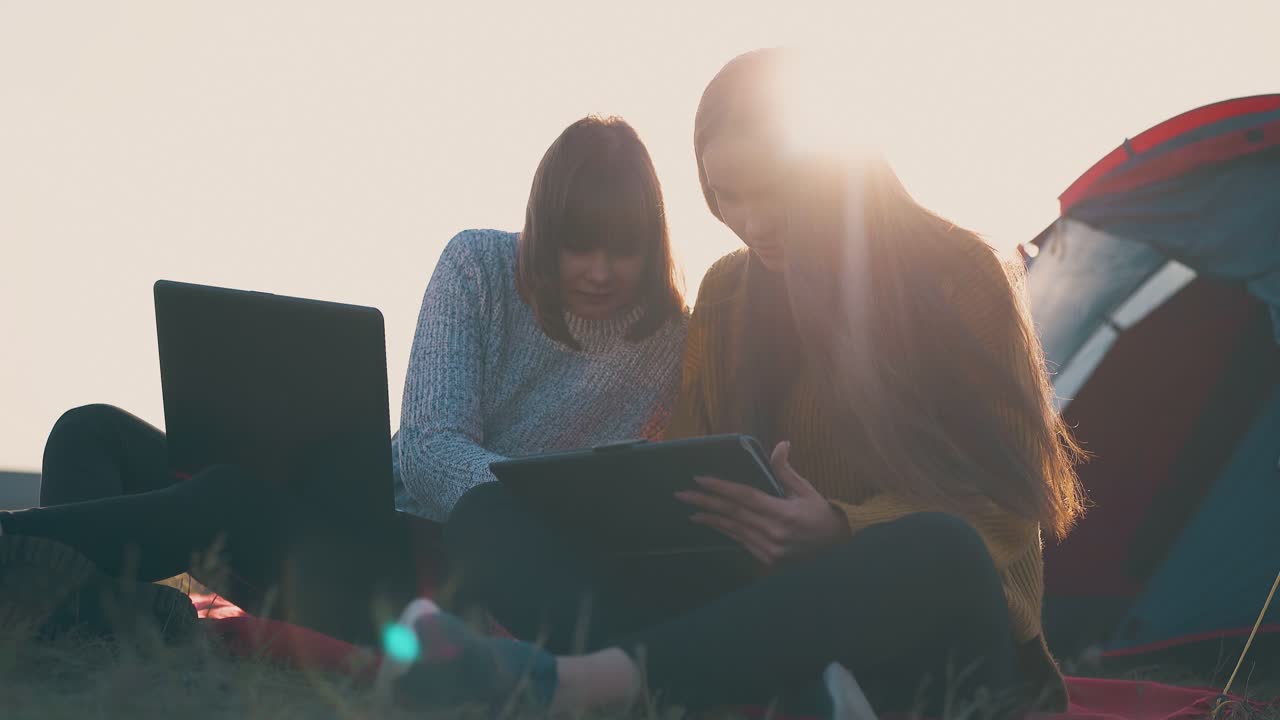 mujeres con tabletas y computadoras portátiles trabajando cerca de la tienda en el campamento