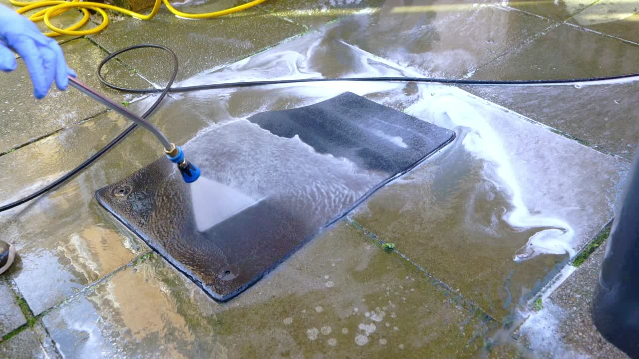 Rinsing small car foot with pressure washer and blue jet wash nozzle - wide shot