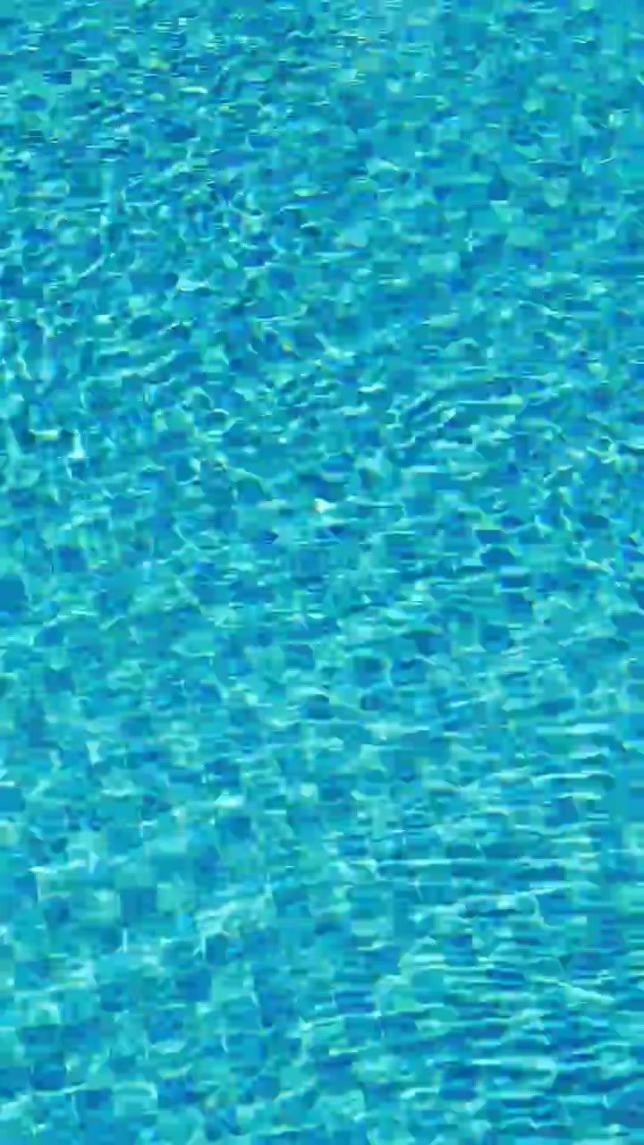Permukaan air kolam renang biru dengan pantulan cahaya matahari yang berkilauan