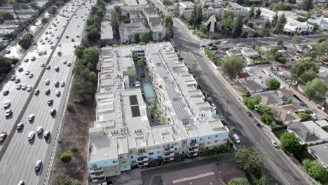 Encore-apartment-complex-next-to-busy-freeway-with-solar-panels-on-roof,-aerial-ascend