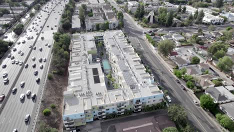 encore apartment complex next to busy freeway with solar panels on roof, aerial ascend