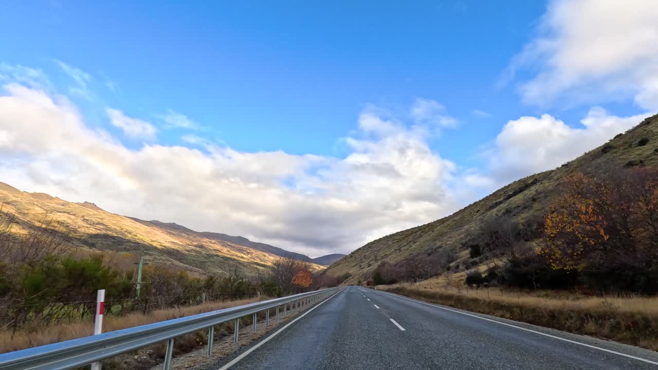 A serene drive through Wanaka's picturesque roads, showcasing vibrant autumn foliage under a bright blue sky