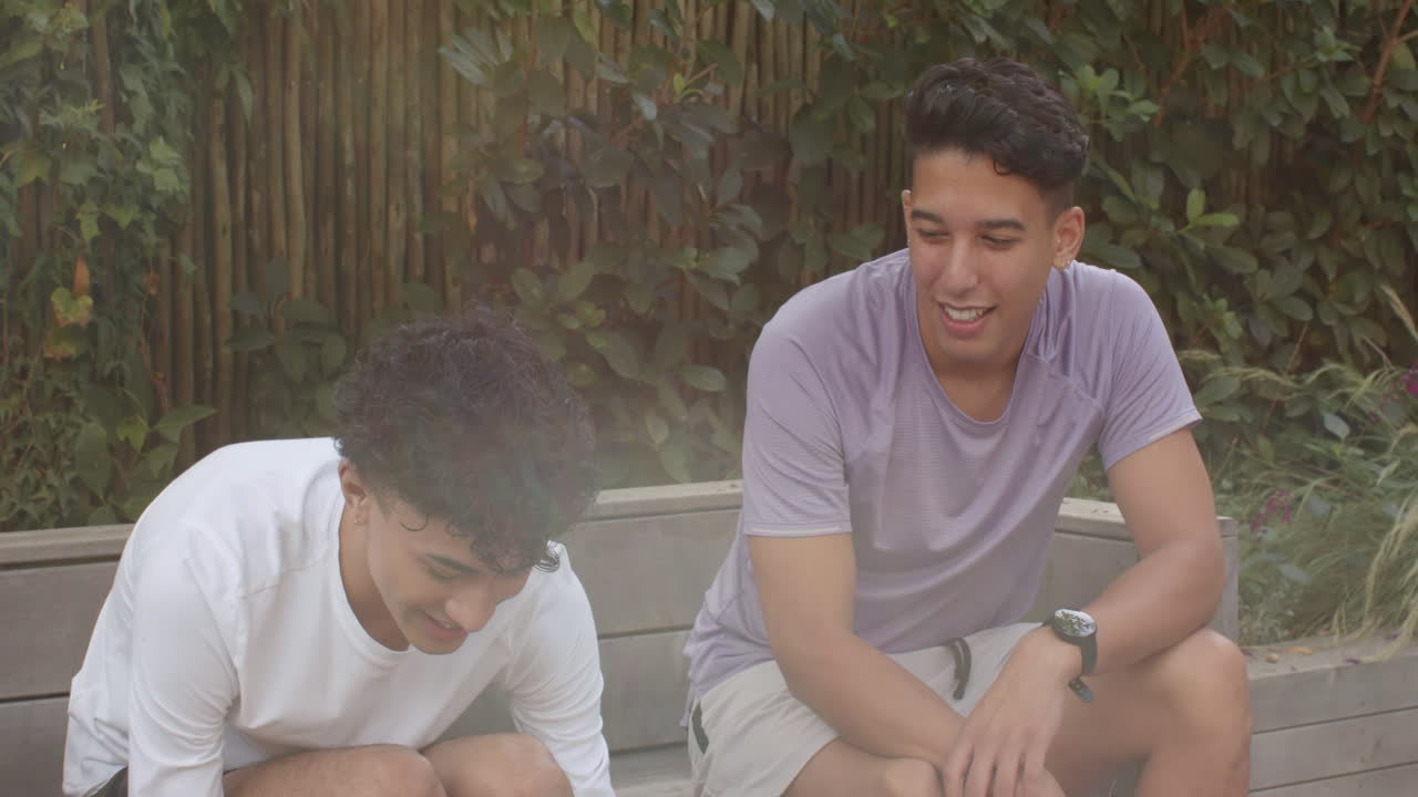 Sitting on bench, multiracial gay couple smiling and enjoying outdoor conversation together