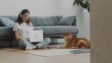 mujer joven que trabaja en su computadora portátil en casa junto a su perro 1