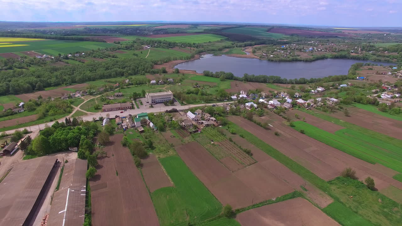 Beautiful scenery of rural area nearby little river. Drone footage over agricultural fields and green forests nearby. View from top.