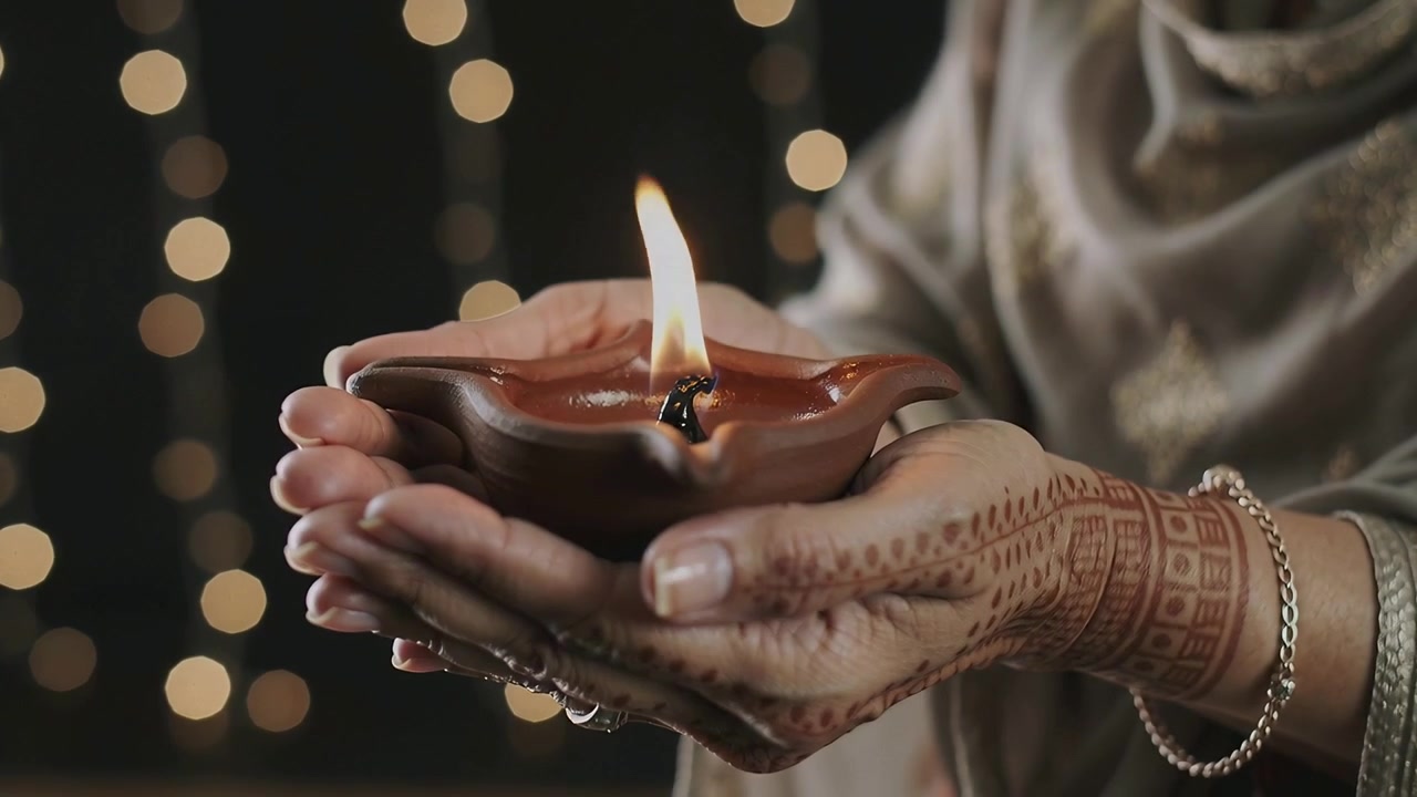 Lighting wick causing woman holding oil lamp at home for ritual offering, henna, embroidered scarf