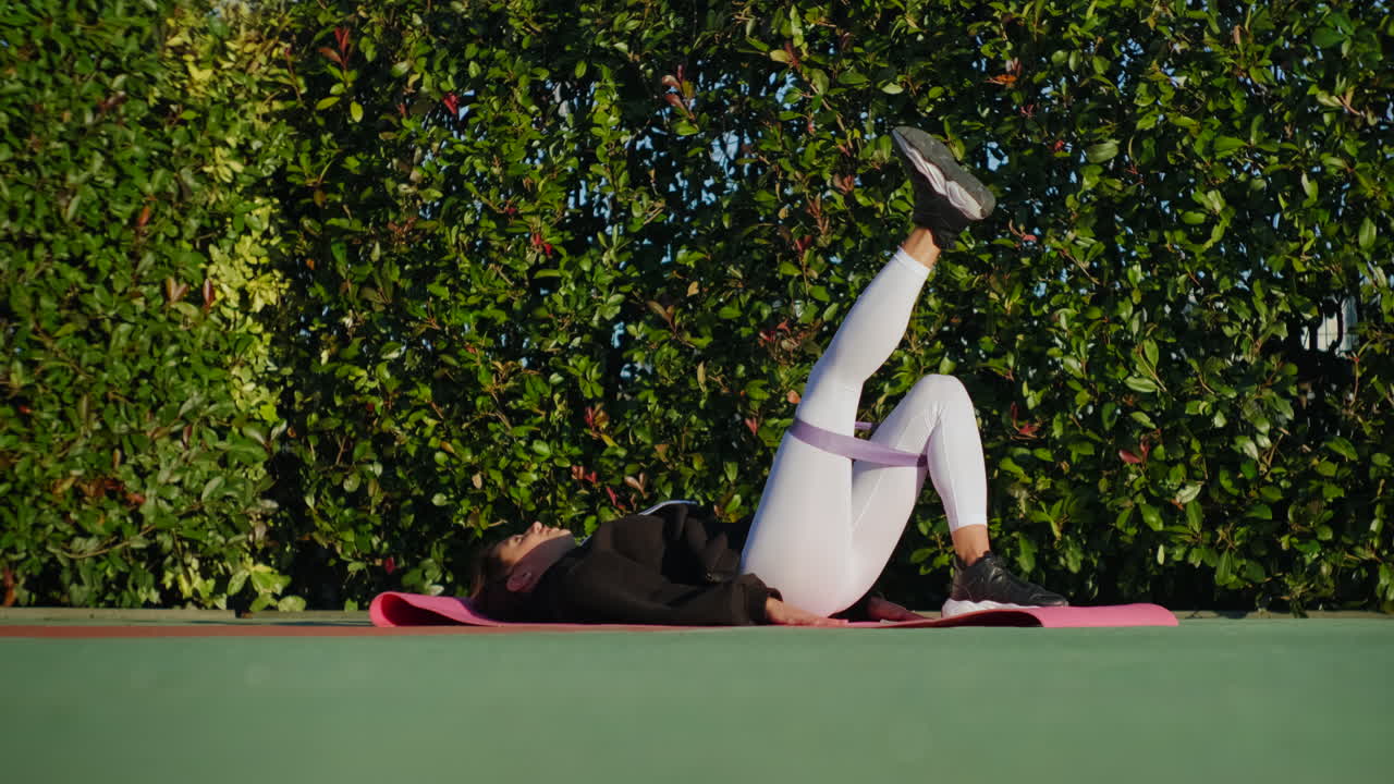 женщина делает поднятия ног с группой сопротивления на открытом воздухе