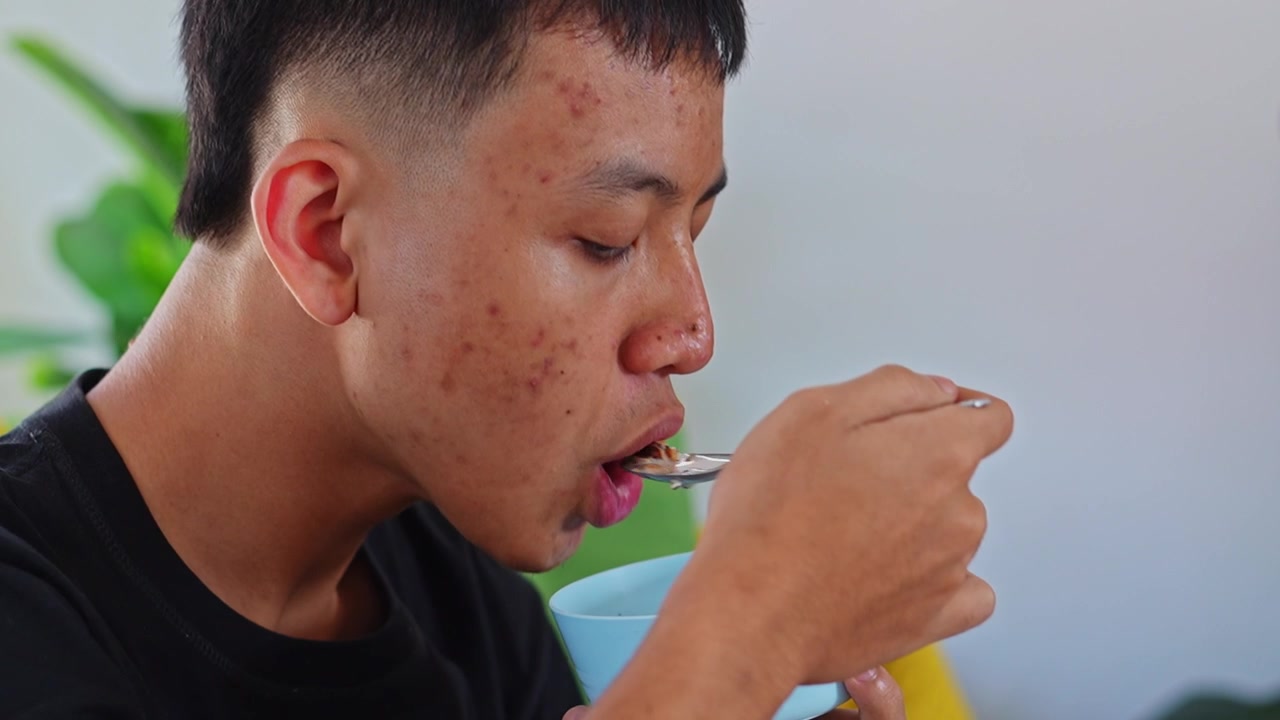 Primo piano di un giovane uomo che gusta granola con latte usando un cucchiaio da una ciotola blu.