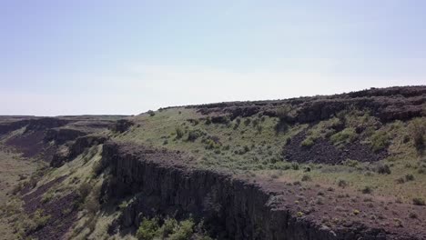 aerial rises past rock cliffs to sagebrush scablands on plateau above