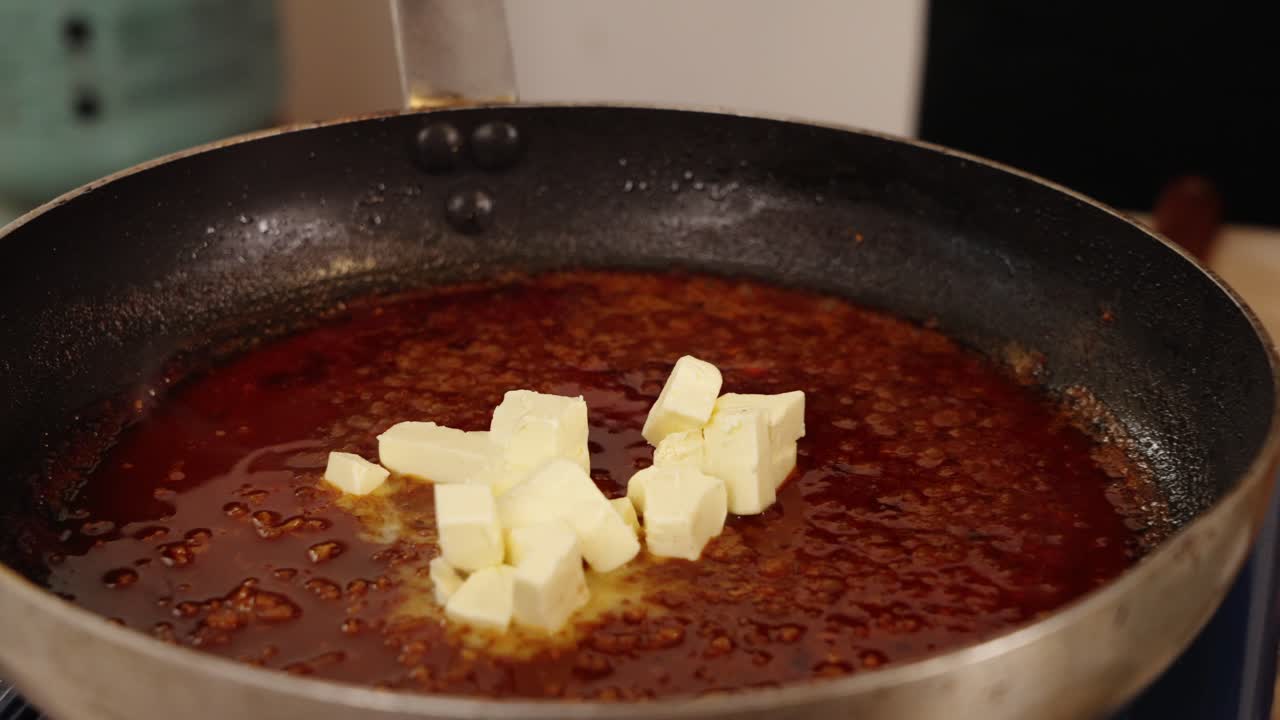 전문 셰프가 장갑을 끼고 도마에서 작은 버터 큐브를 집어 얕은 프라이팬에 지글거리는 뜨거운 칠리 기름에 옮기고 추가합니다.