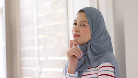 Portrait-of-smiling-biracial-woman-in-hijab-at-home-with-copy-space,-slow-motion