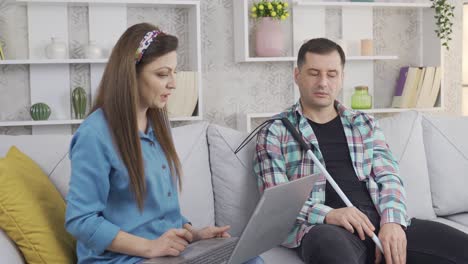 su esposa le dice algo al hombre con discapacidad visual mirando la computadora portátil.