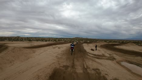 skilled adventurists take jumps on a dirt racetrack in the mojave desert as seen in slow motion from a first-person drone