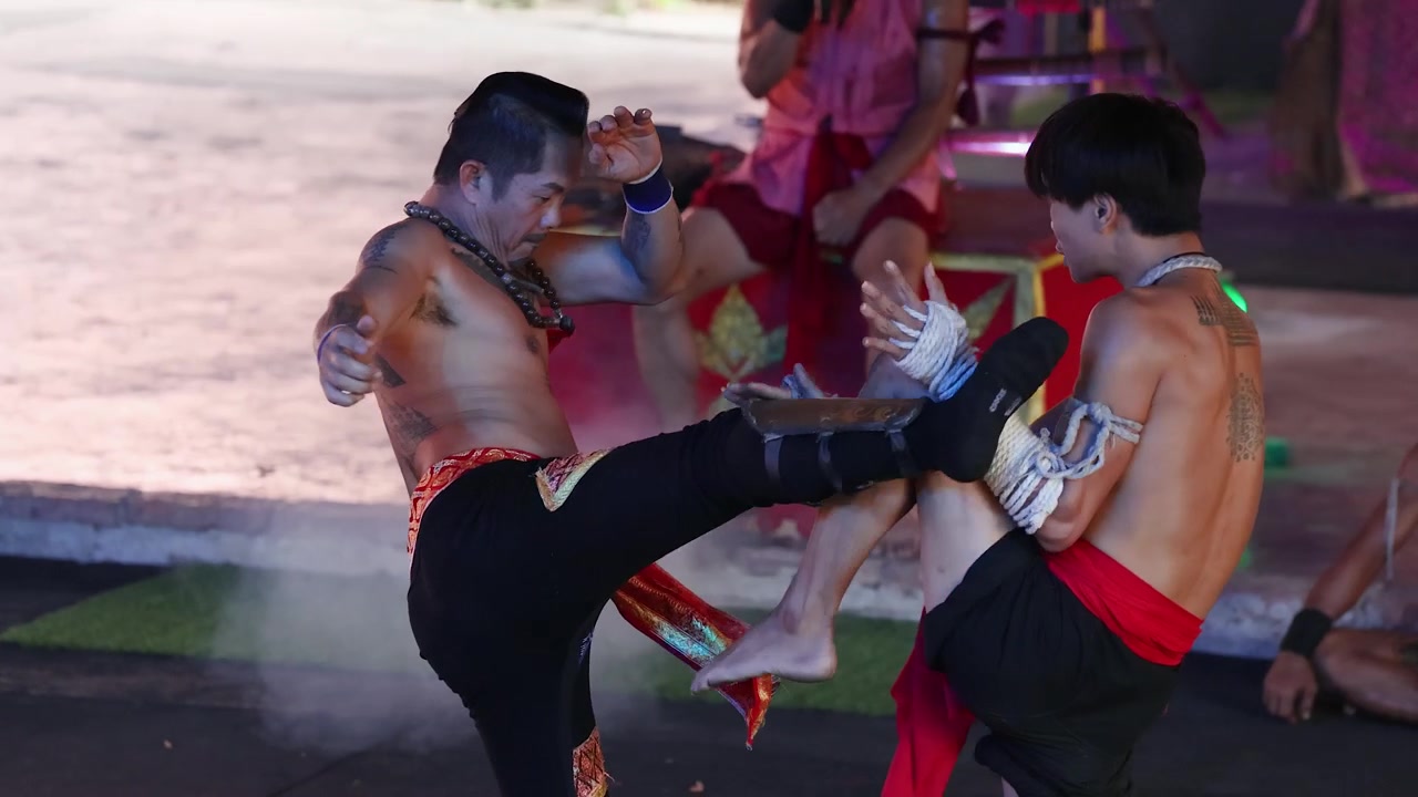 Artisti marziali tatuati eseguono colpi tradizionali di kickboxing e manovre difensive in un ring all'aperto