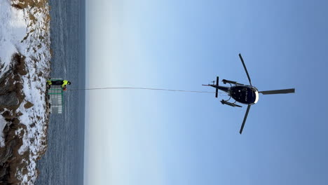 vertical shot of a helicopter with a worker hooking container on a longline, during strong wind in the arctic polar circle