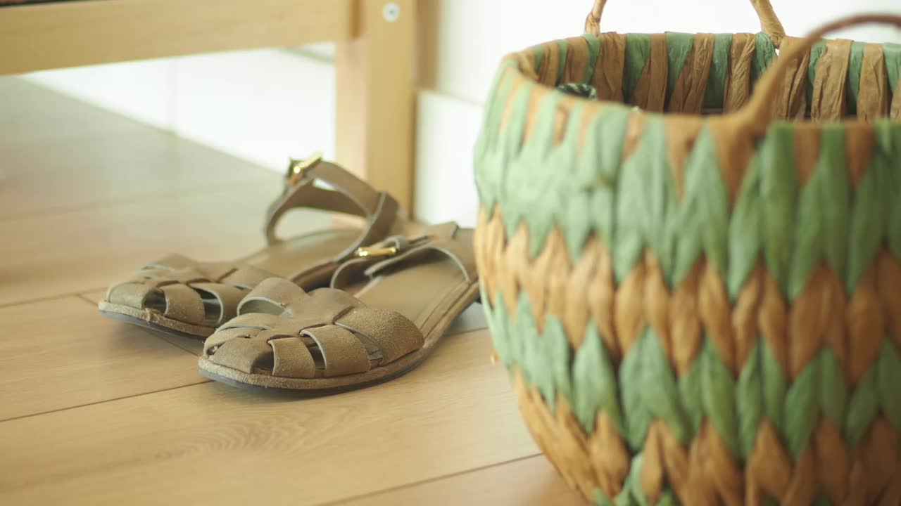 A pair of brown sandals on a wooden floor next to a woven basket