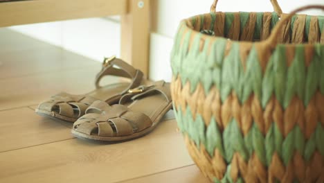 a pair of brown sandals on a wooden floor next to a woven basket