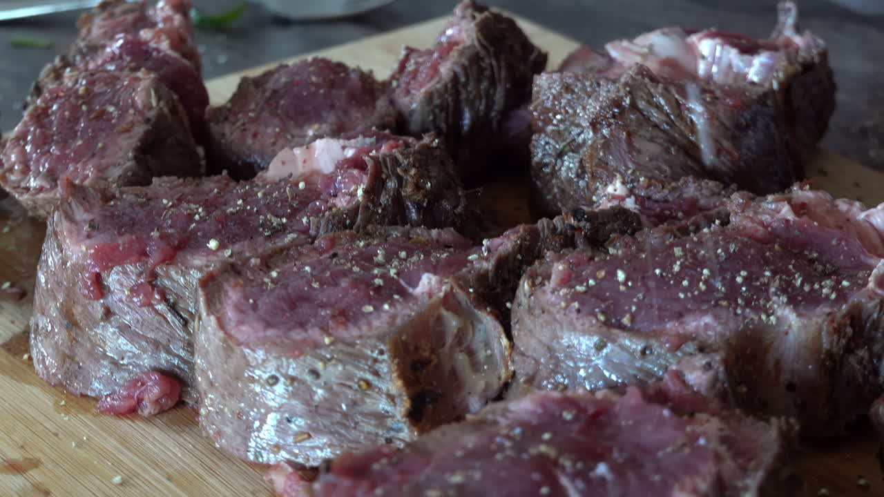 Woman salting a piece of cut up red meat on a wooden cutting board