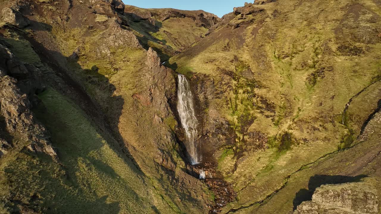 Aerial view of a waterfall cascading down rocky cliffs in northern Iceland, surrounded by moss-covered terrain and untouched wilderness.