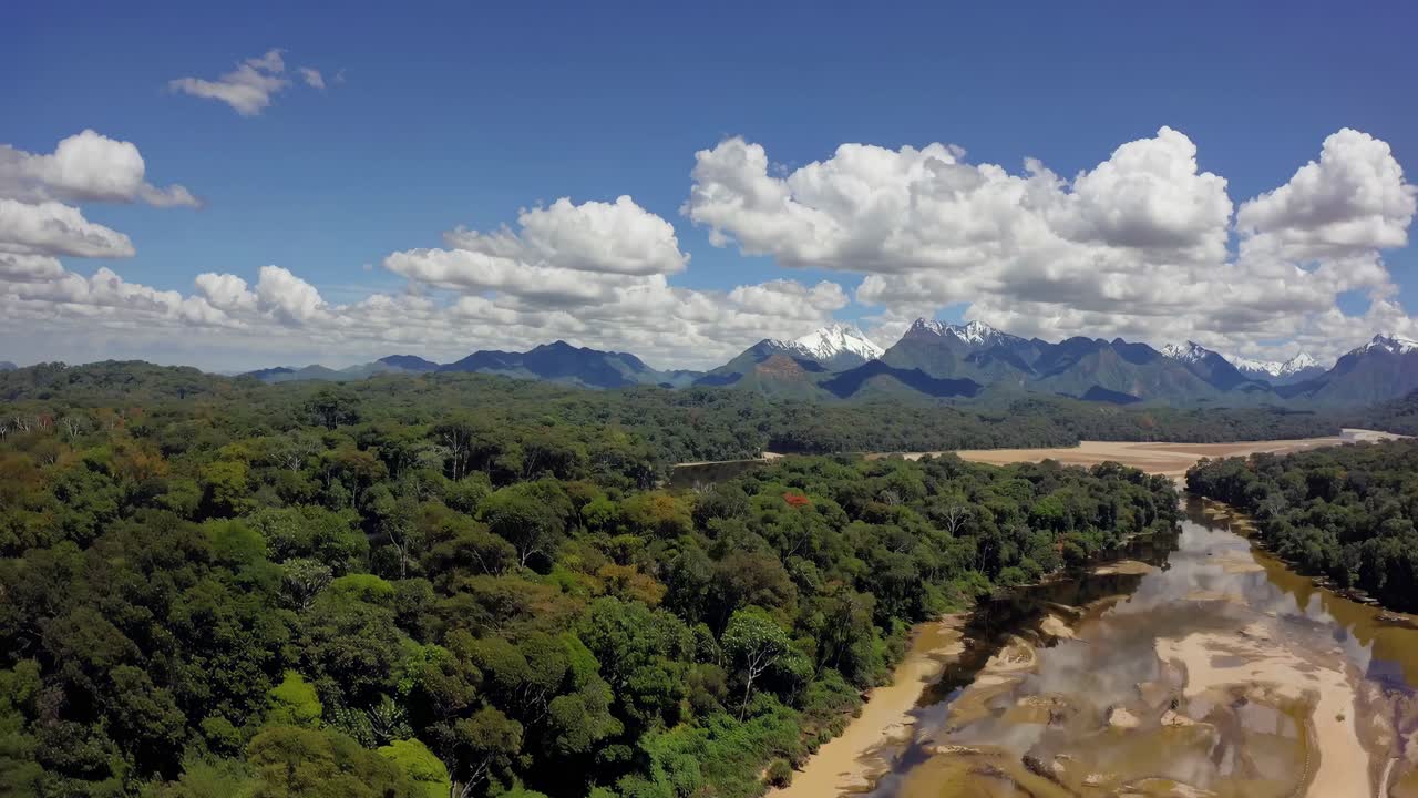 Aerial video captures lush rainforest and winding river with distant mountains under a bright blue