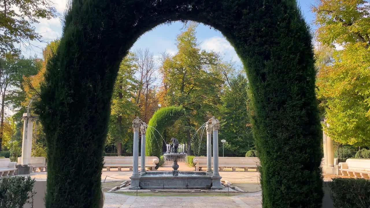 View of the Arpias fountain in the gardens of the Aranjuez palace framed in a vegetal arch in Arizona we see the water jets and the sculpture of the child between columns on a beautiful morning