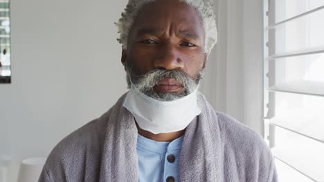 senior man with face mask on his chin at home