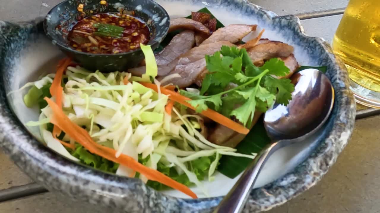 A vibrant salad with sliced meat, fresh herbs, and a glass of beer on the side.
