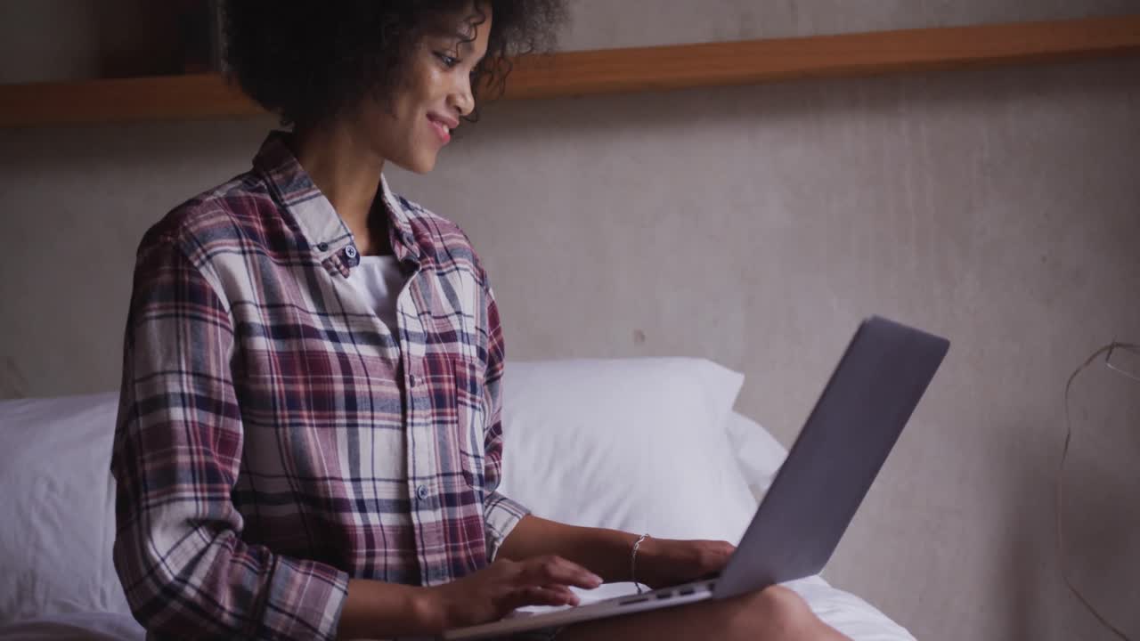 Mixed race woman using computer in bedroom