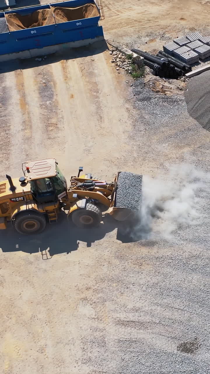Asphalt plant with running bulldozer. The plant serves the needs of road construction. Industrial machine is loading rubbles. Aerial view. Vertical video