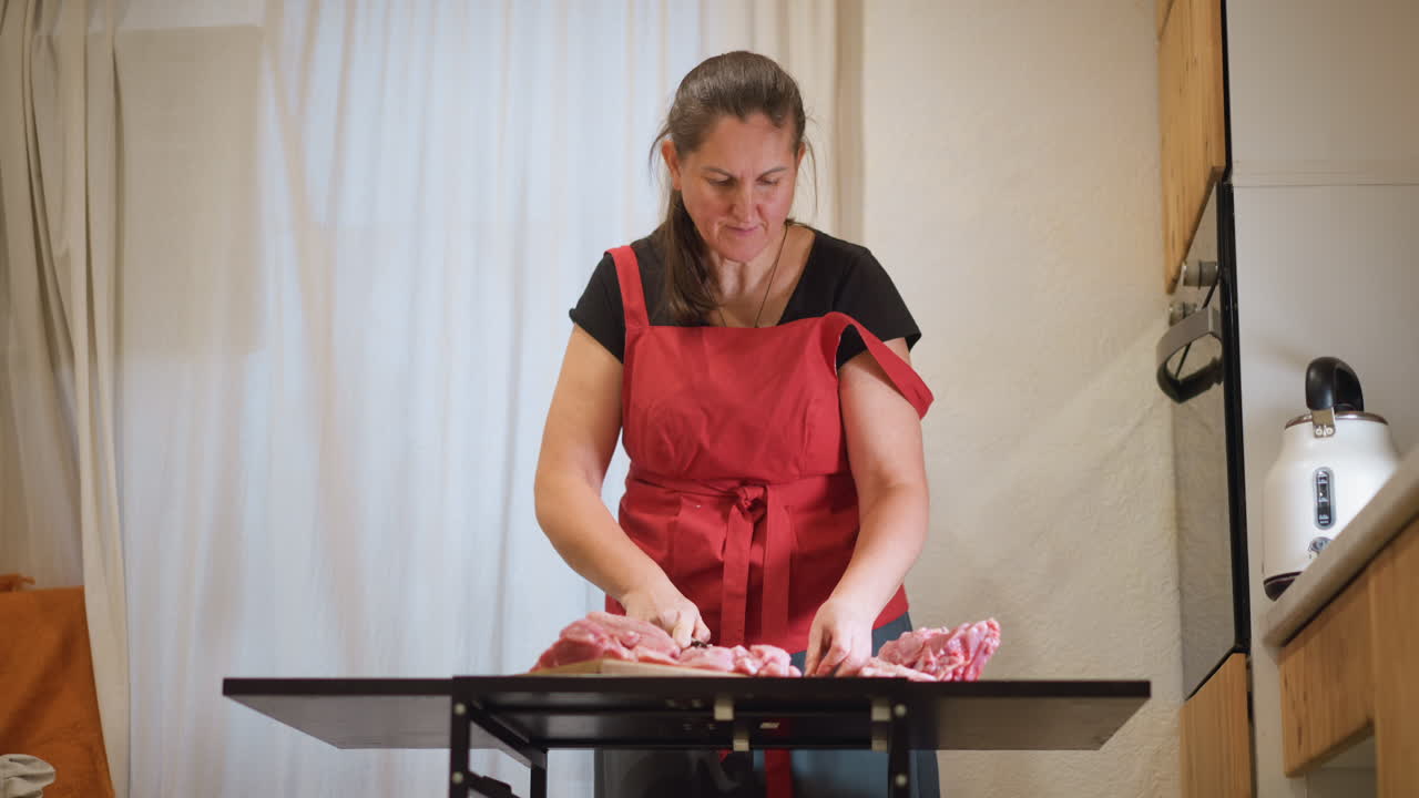Cocinera casera caucásica enseñando técnica, habilidades con el cuchillo paso a paso, ingredientes organizados en tabla de cortar, delantal rojo, encuadre apto para cámara y luz natural brillante, preparación práctica de comidas