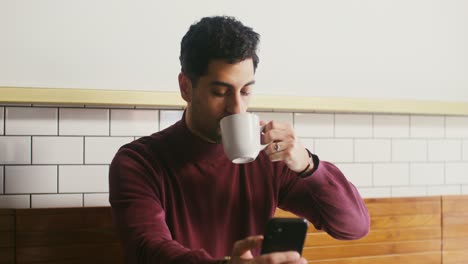 hombre bebiendo café y usando un teléfono inteligente en una cafetería