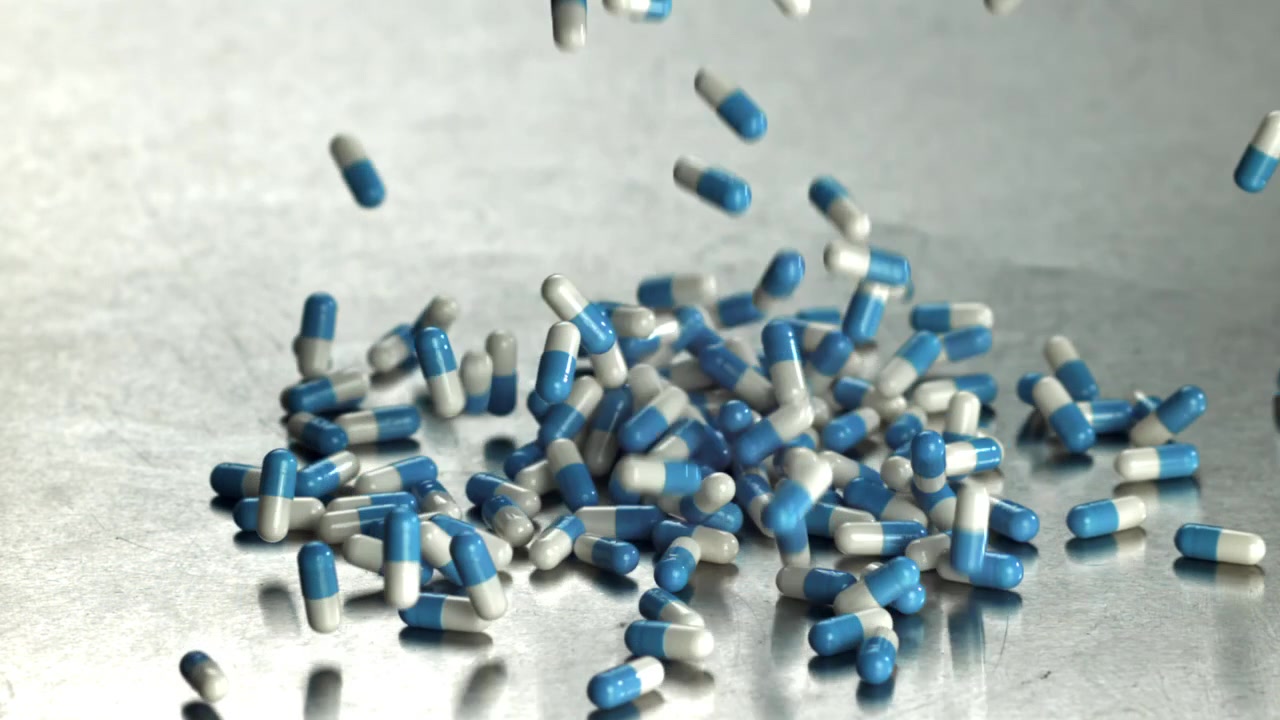 Capsule blu e bianche che cadono e si disperdono su superficie metallica in movimento rallentato