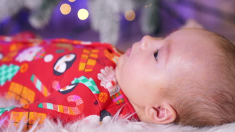 sweet baby boy in red christmas clothes lies his side to the camera. beautiful baby with plump cheeks close up. blurred backdrop.