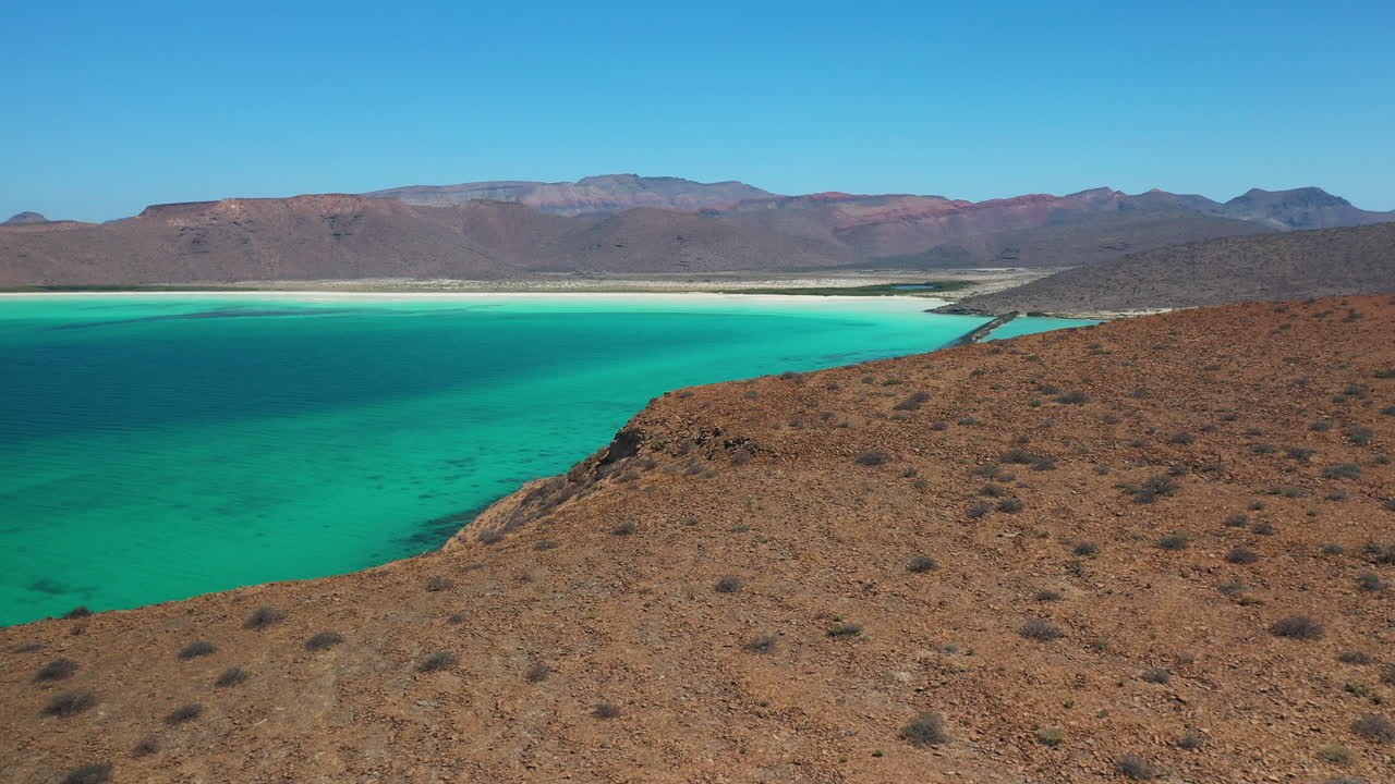 빨간 언덕, 청록색 바다, 하얀 모래 해변을 지나 언덕 위로 내려가는 발란드라 해변의 영화 같은 드론 샷