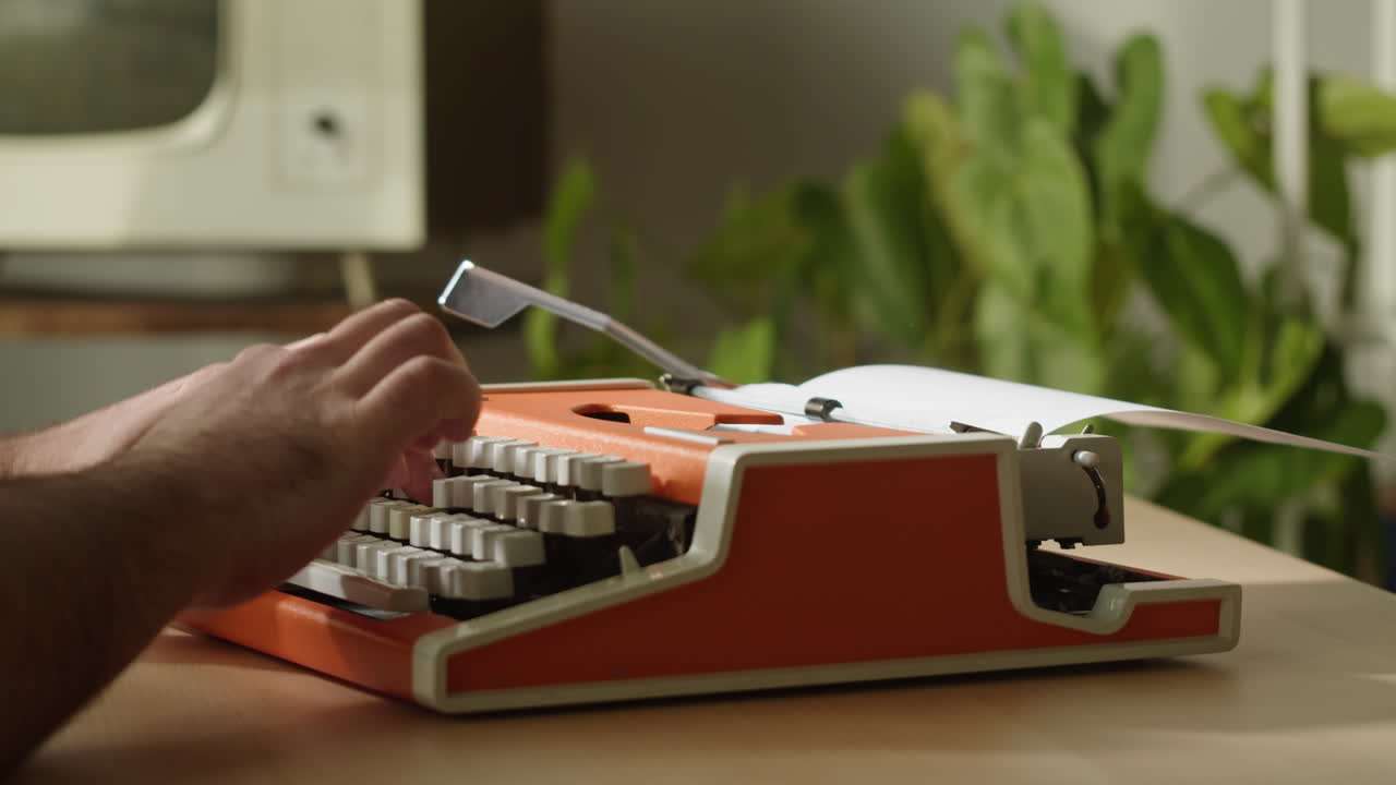 Mani che digitano su una macchina da scrivere vintage arancione.