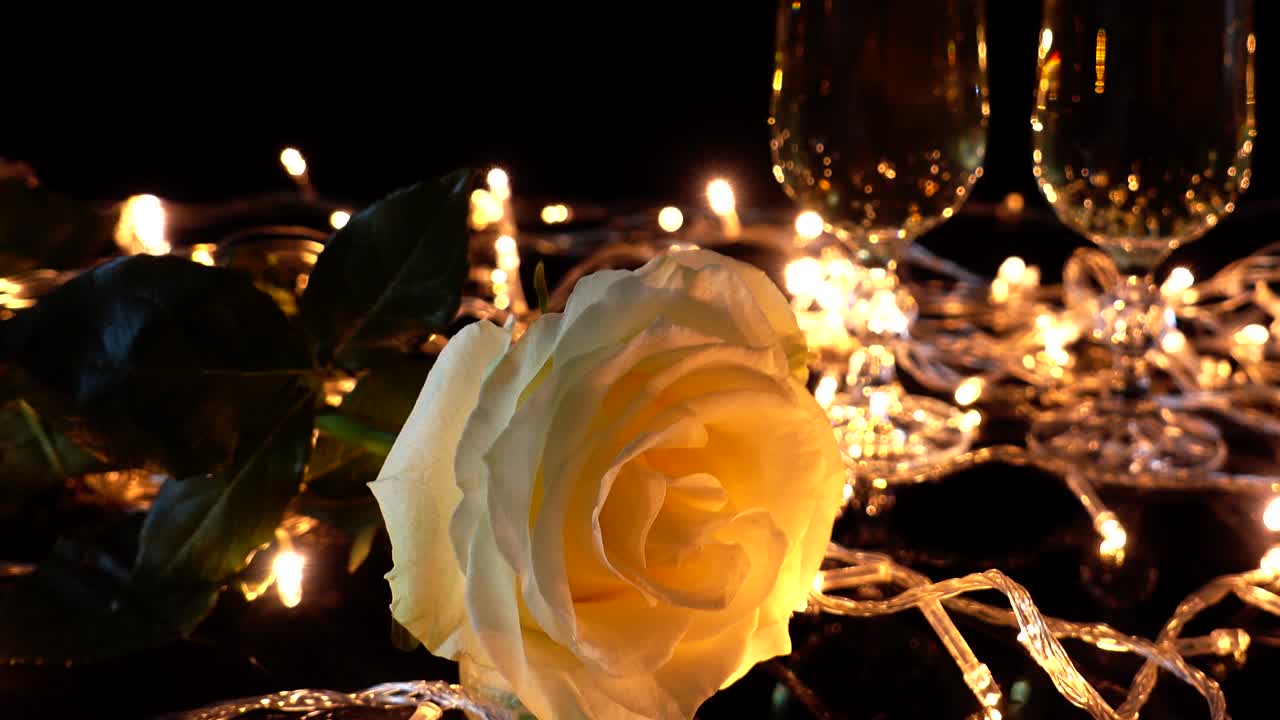 Calici da champagne e una rosa sullo sfondo di ghirlande luminose