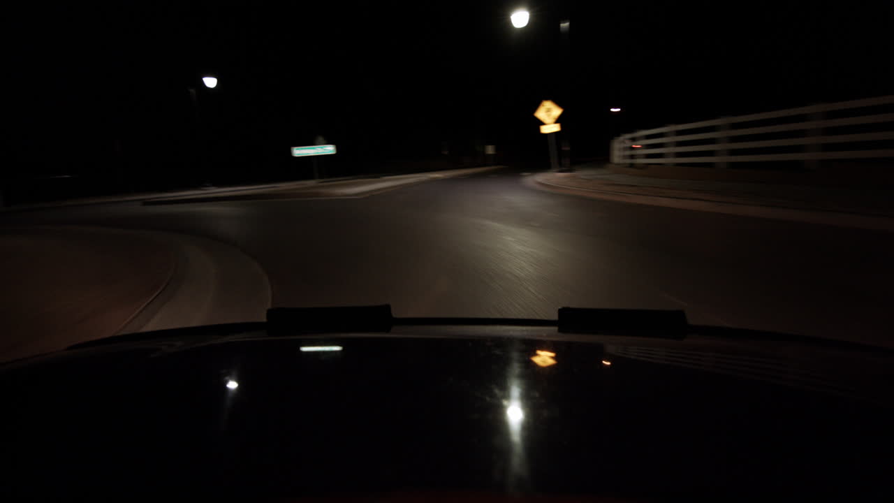 A hood of a car point of view driving at night driving around a round about