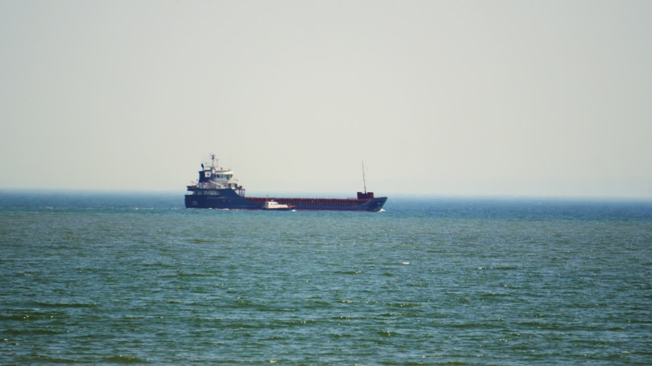 Huge Container Ship After Emptying Cargo at Nearby Port with Support Vessel as it Exits Swansea Bay in South Wales. Headed to Destination to Pick Up Goods for Importing and Exporting Shipping.