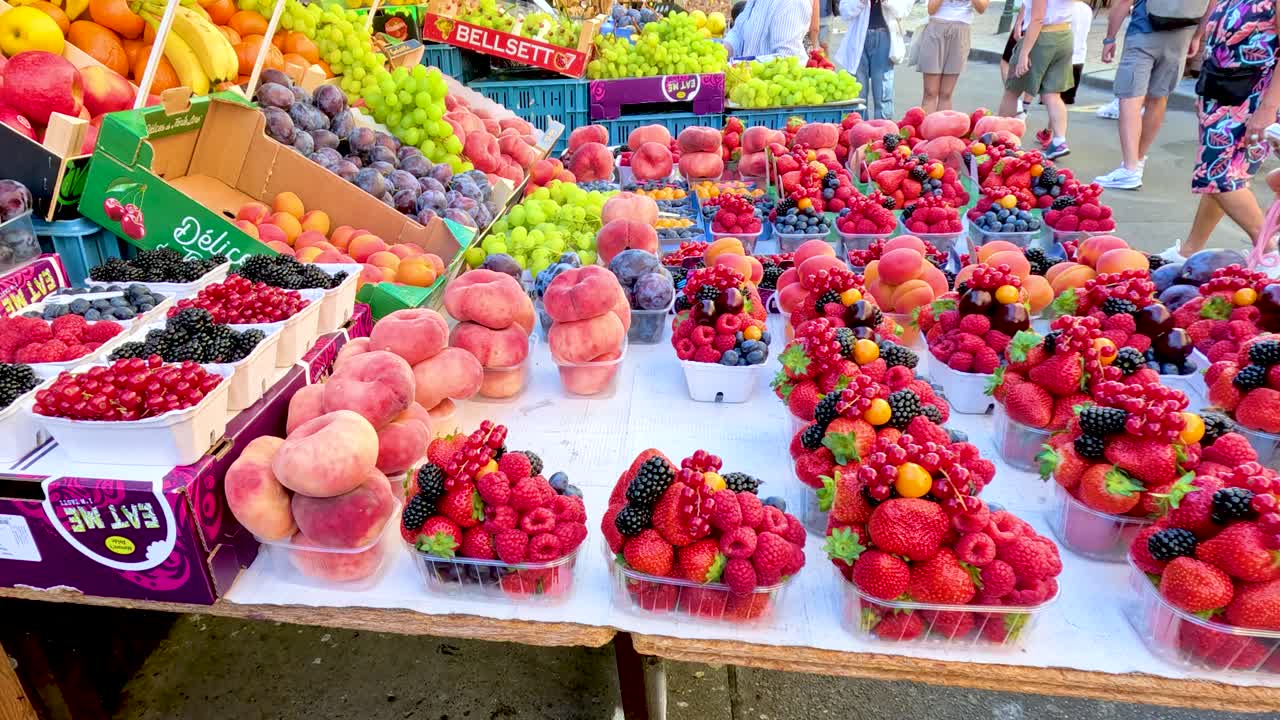 Colorful assortment of peaches, berries, and grapes arranged on a market stall in Prague, captured with smooth panning camera movement and natural daylight