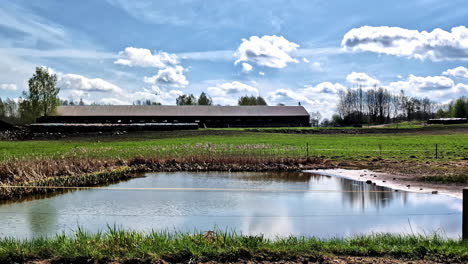 small farm pond and barn under blue sky in spring viewed from a driving car