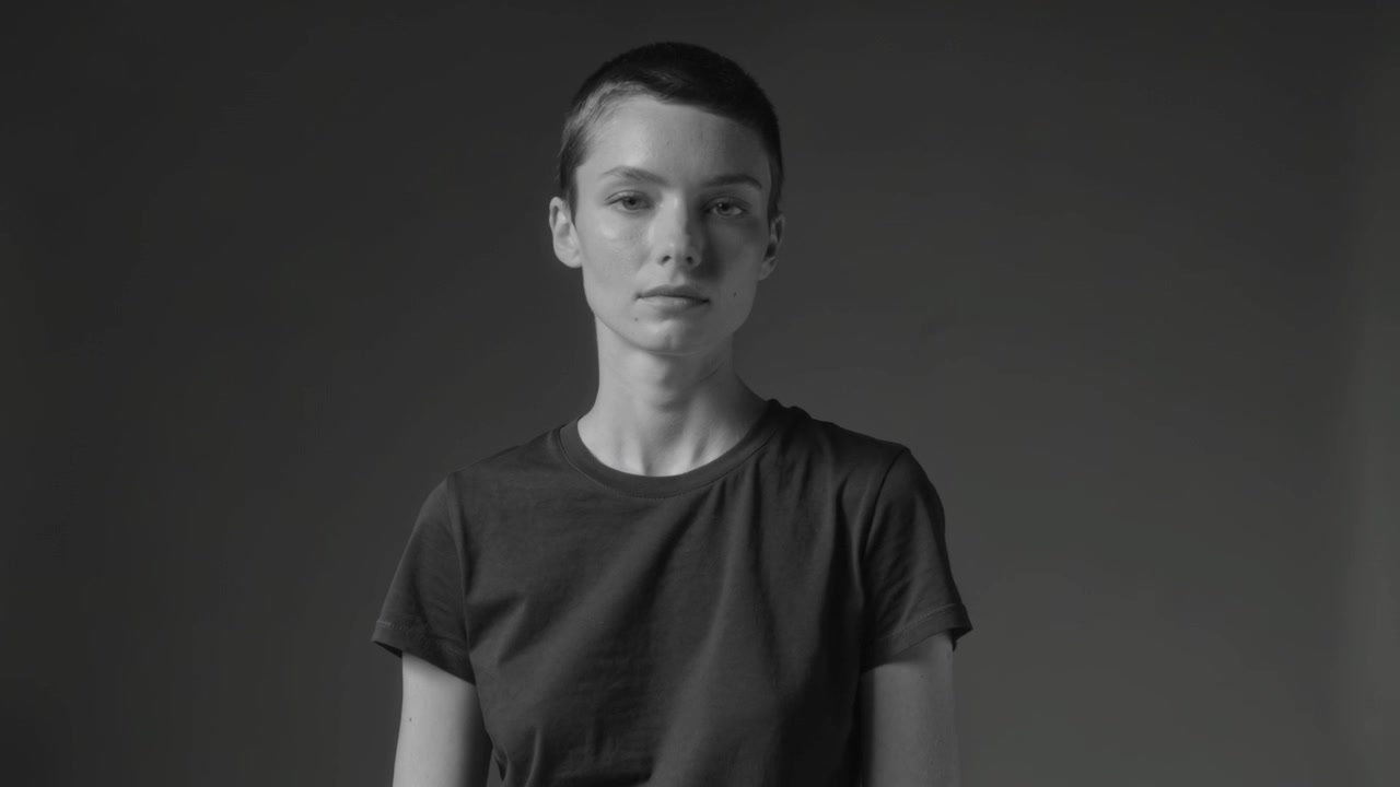 Standing model moving head and eyes at studio backdrop under lights, camera capturing in dark tee