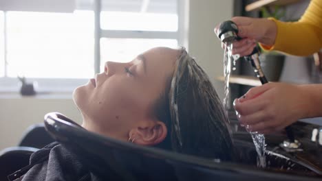 hands of caucasian female hairdresser washing hair of relaxed female customer at hair salon