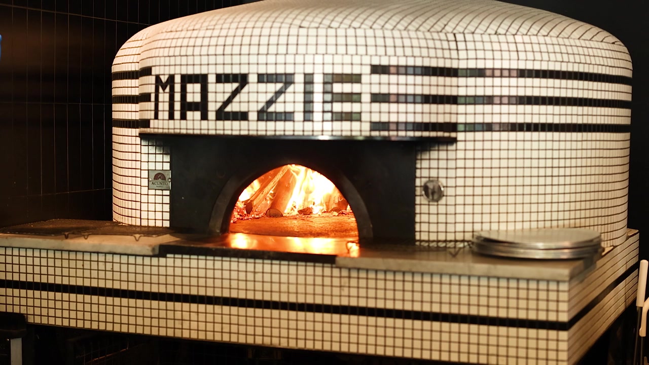 Inquadratura media statica di un forno per pizza napoletana piastrellato con fiamme arancioni brillanti che bruciano all'interno.