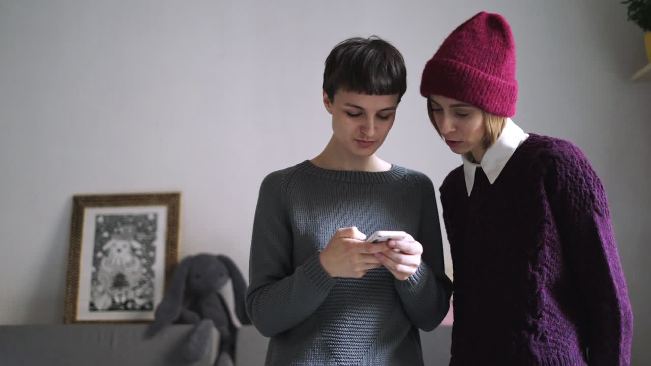 dos mujeres elegantes usando un teléfono móvil en el interior de la casa. amigas smartphone
