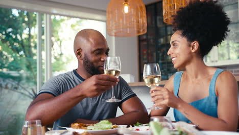 Pareja-Sentada-Alrededor-De-La-Mesa-En-Casa-Haciendo-Aplausos-Con-Vino-Antes-De-La-Comida