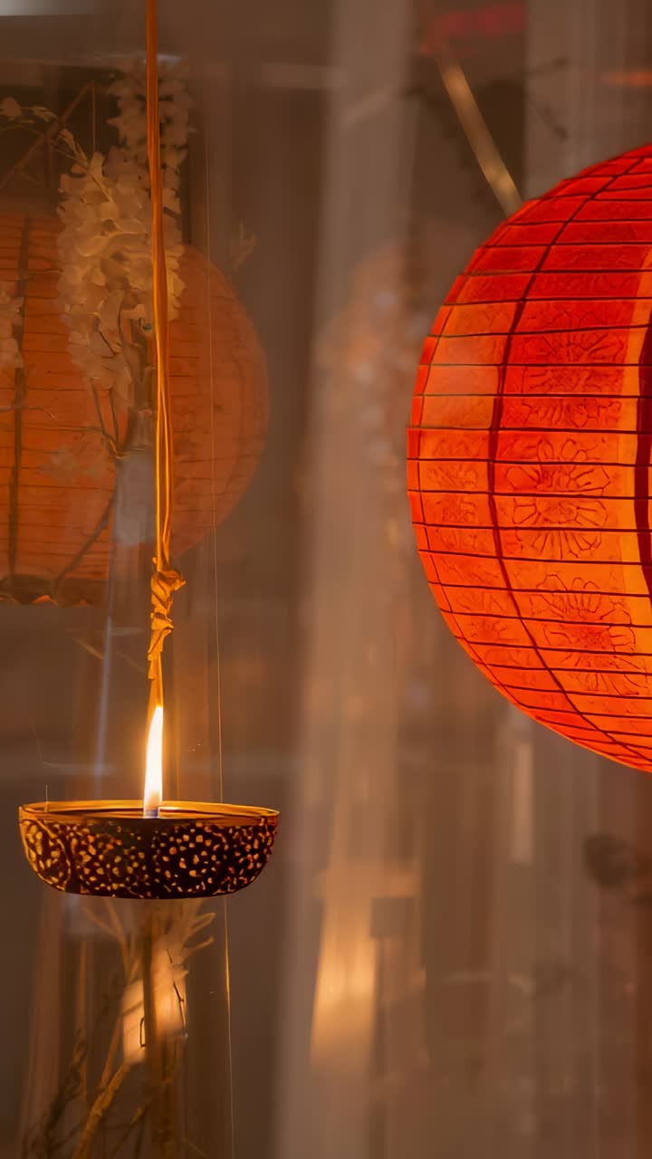 Vertical video: Flickering oil lamp with lit wick lighting red lantern by glass pane, garland decor