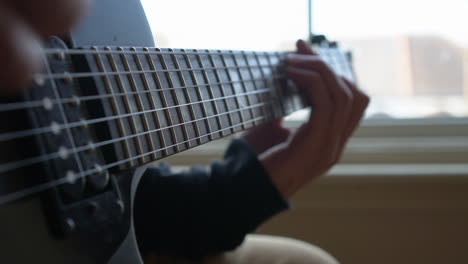 man practising a vintage black electric guitar, rehearsing chords, solos and octaves in a natural light environment.