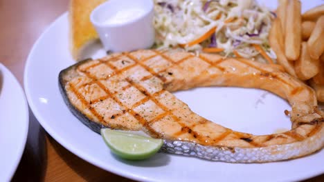detail einer schönen platte mit gegrilltem lachsfilet, pommes frites und salat