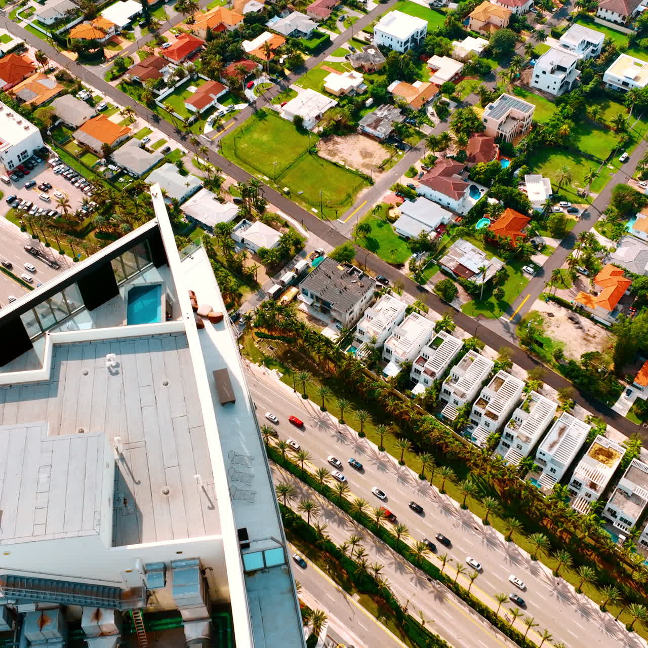 Footage above the top of the high-rise building with a swimming-pool and lounge area on. Busy highway at the foot of the house and low-rise architecture below. Top view on Miami Beach, Florida, USA.